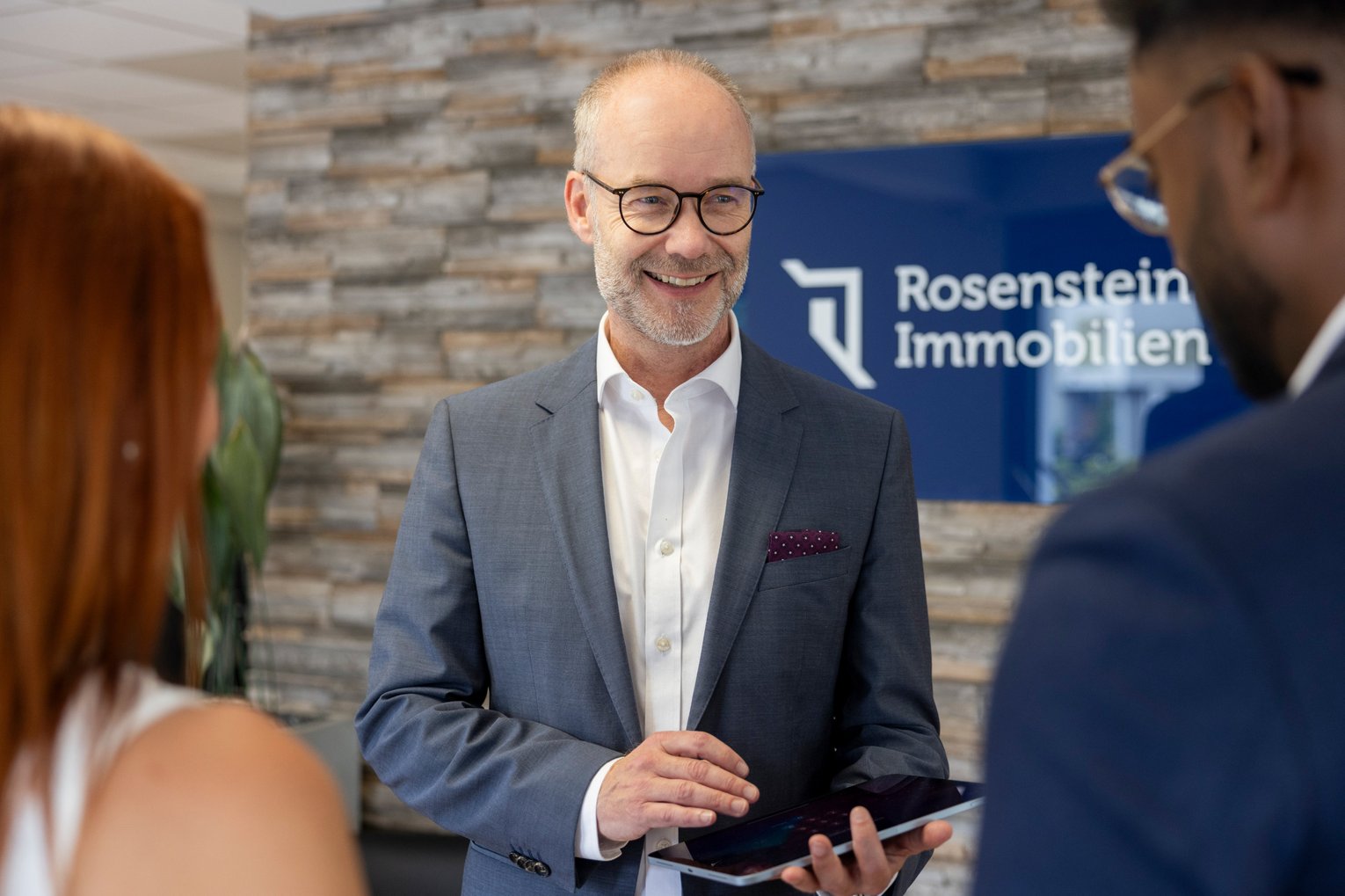 Beratungsgespräch bei Rosenstein Immobilien Immobilienberater im Gespräch mit Kunden vor dem Schild von Rosenstein Immobilien